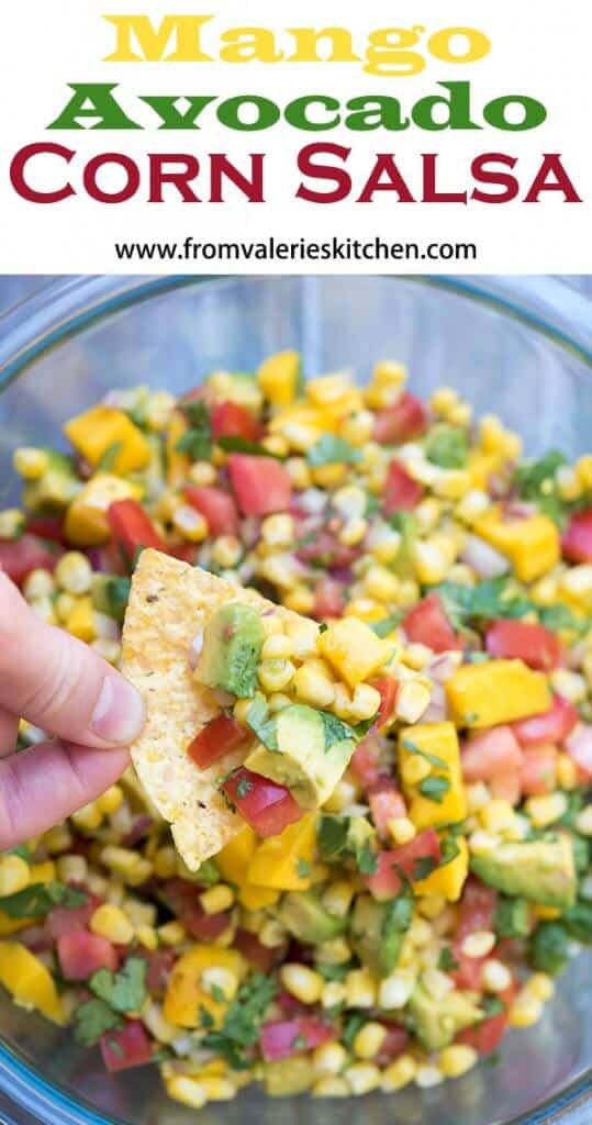 A hand holds a tortilla chip filled with Mango Avocado Corn Salsa over a serving bowl with overlay text.