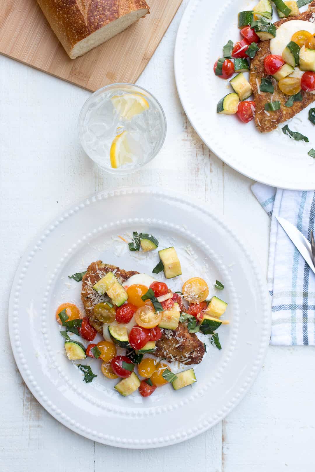 Two white plates with a serving of chicken with colorful vegetables over the top.