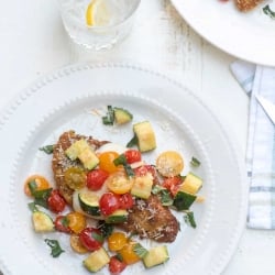 Chicken topped with vegetables and Parmesan on a white plate.