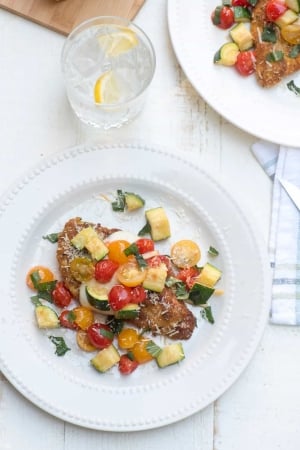 Chicken topped with vegetables and Parmesan on a white plate.