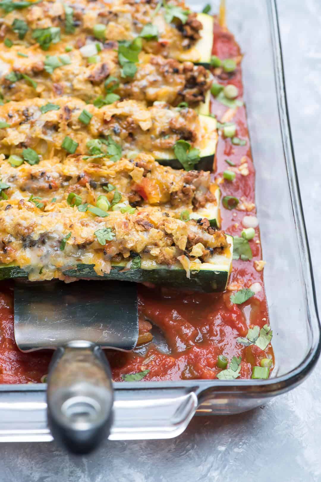 A spatula lifts one of the zucchini boats from the casserole dish.