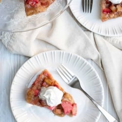 A rhubarb cake topped with whipped cream on a white plate.
