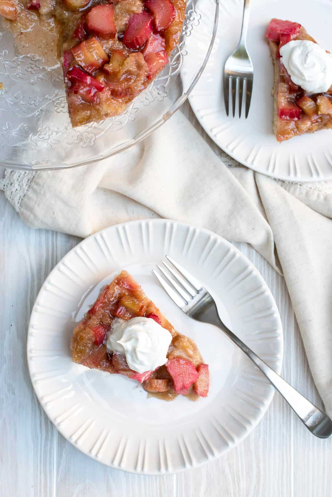 A rhubarb cake topped with whipped cream on a white plate.