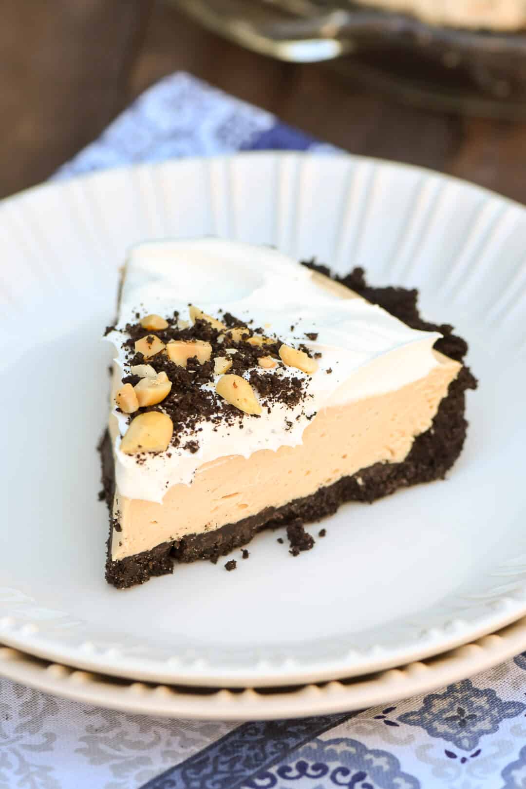 A slice of Frozen Peanut Butter Pie topped with crushed Oreos and peanuts on a white serving plate.