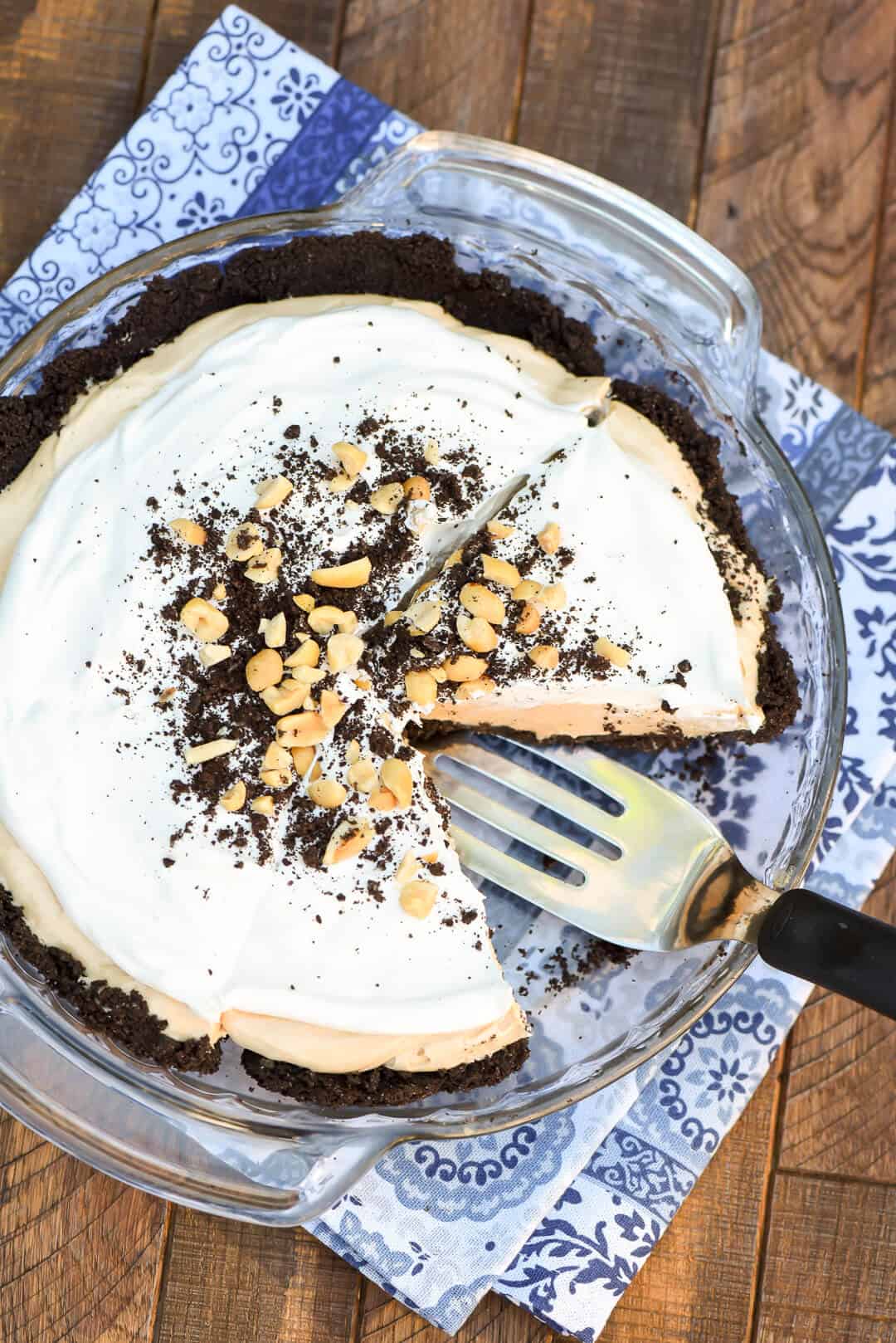 An over the top image showing a spatula lifting a slice of pie from the pie dish that sits on a blue cloth.