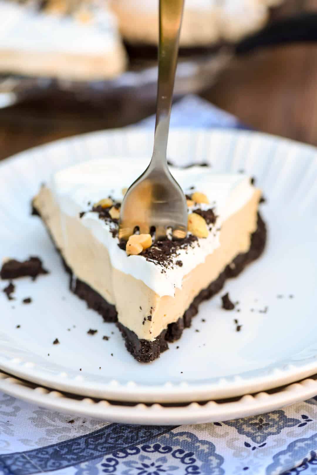 A piece of layered pie on a plate with a fork stuck in it.