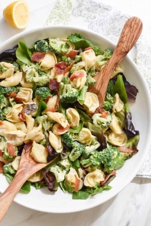 A bowl of spinach topped with tortellini and broccoli.