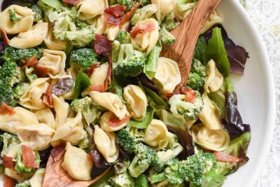 A bowl of spinach topped with tortellini and broccoli.