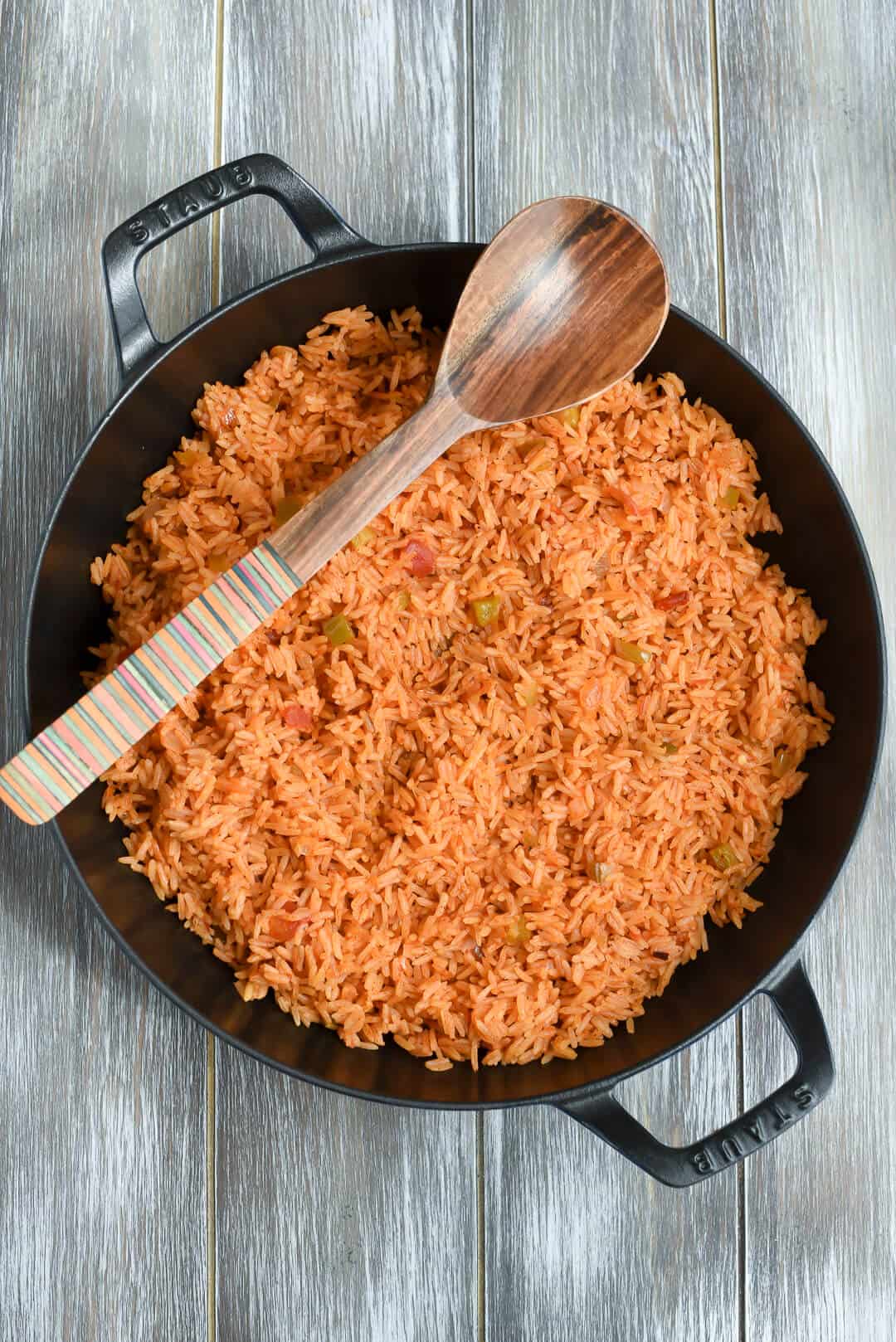 A skillet full of Salsa Rice with a wooden spoon resting over the top.