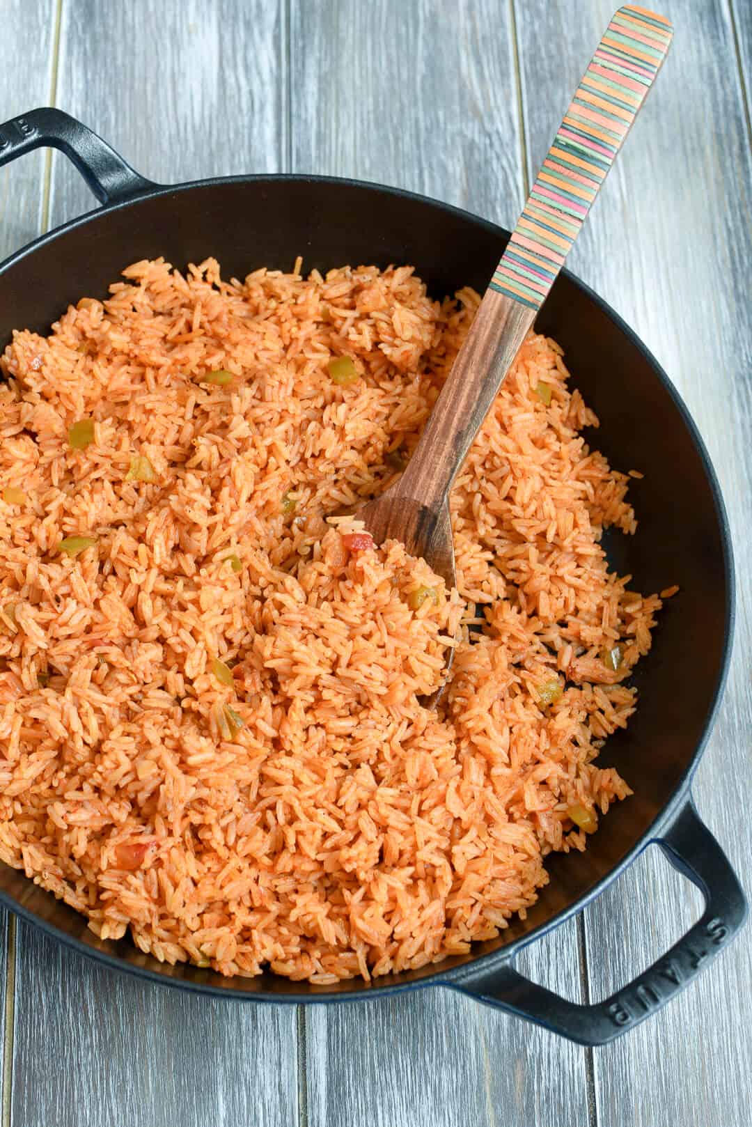 A wooden spoon digs into the rice in the skillet.