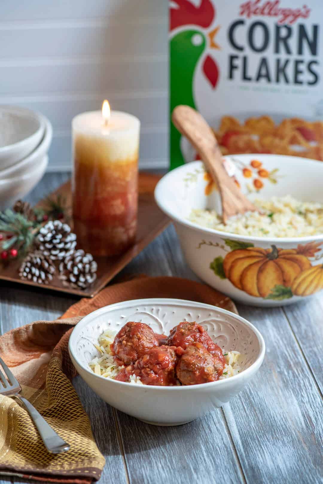 A serving of the meatballs in a white bowl with the rice pilaf and a box of Kellogg's Corn Flakes in the background.