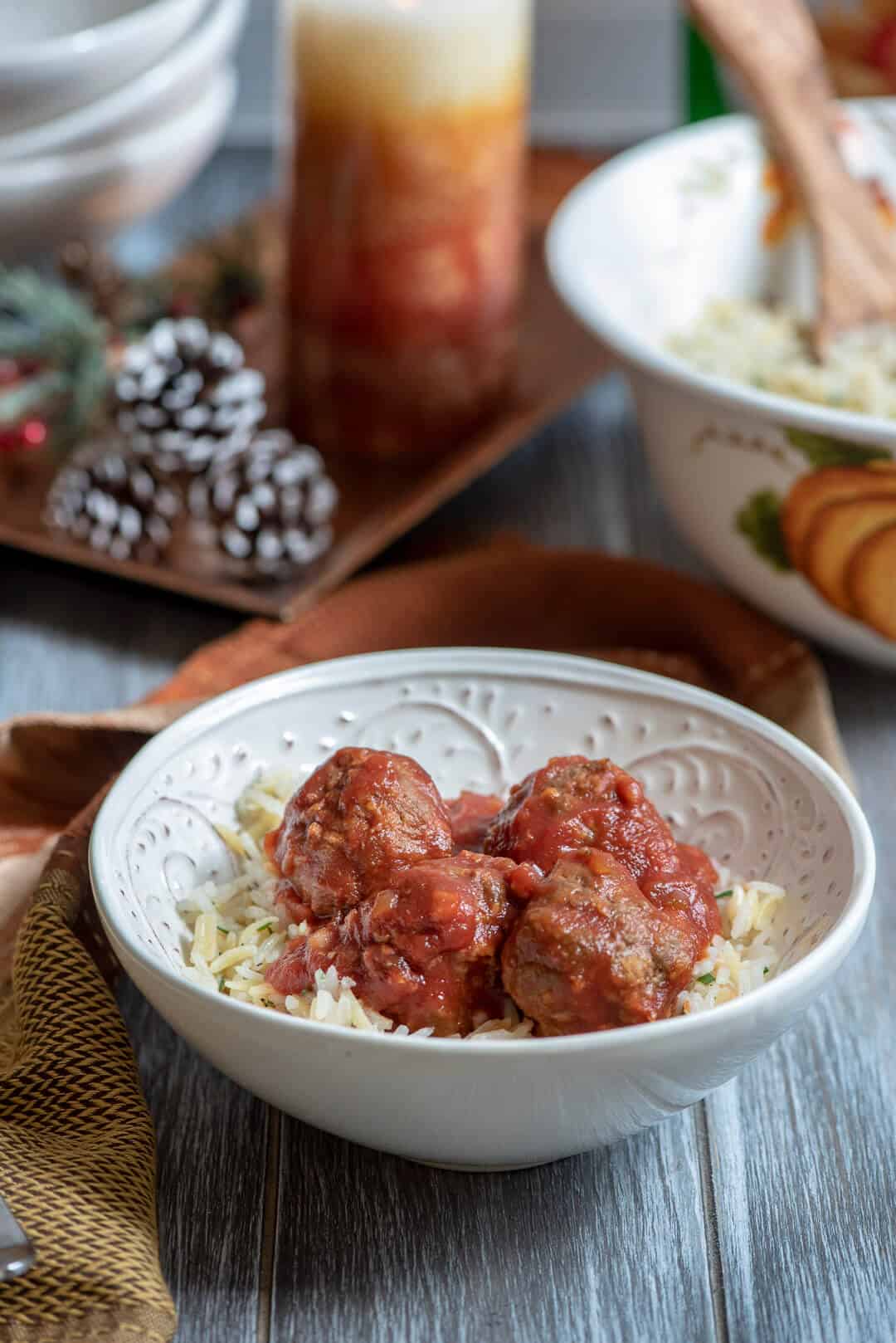 A bowl of rice topped with meatballs with pine cones and a candle in the background.