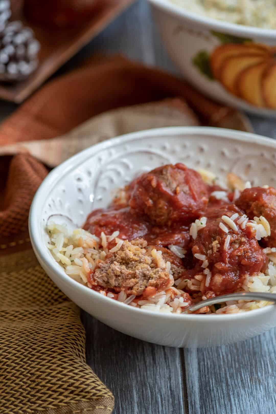 A fork breaks into one of the meatballs in the white bowl.