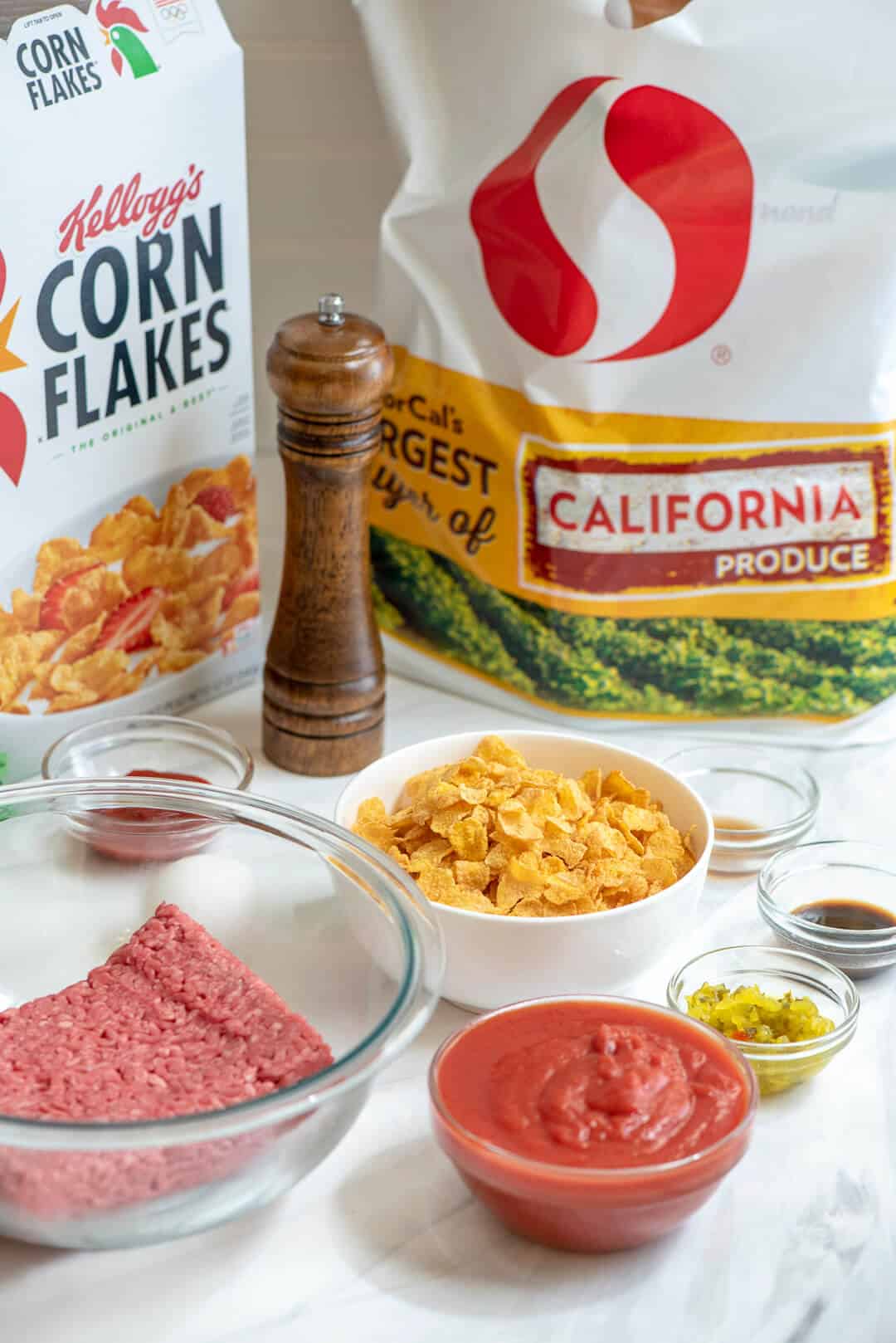 The Ingredients for Good and Spicy Meatballs in front of a white plastic Safeway grocery bag and a box of Kellogg's Corn Flakes.