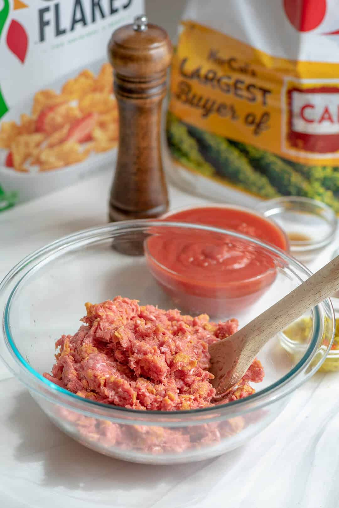 Ground beef is added to the bowl and mixed with a wooden spoon.