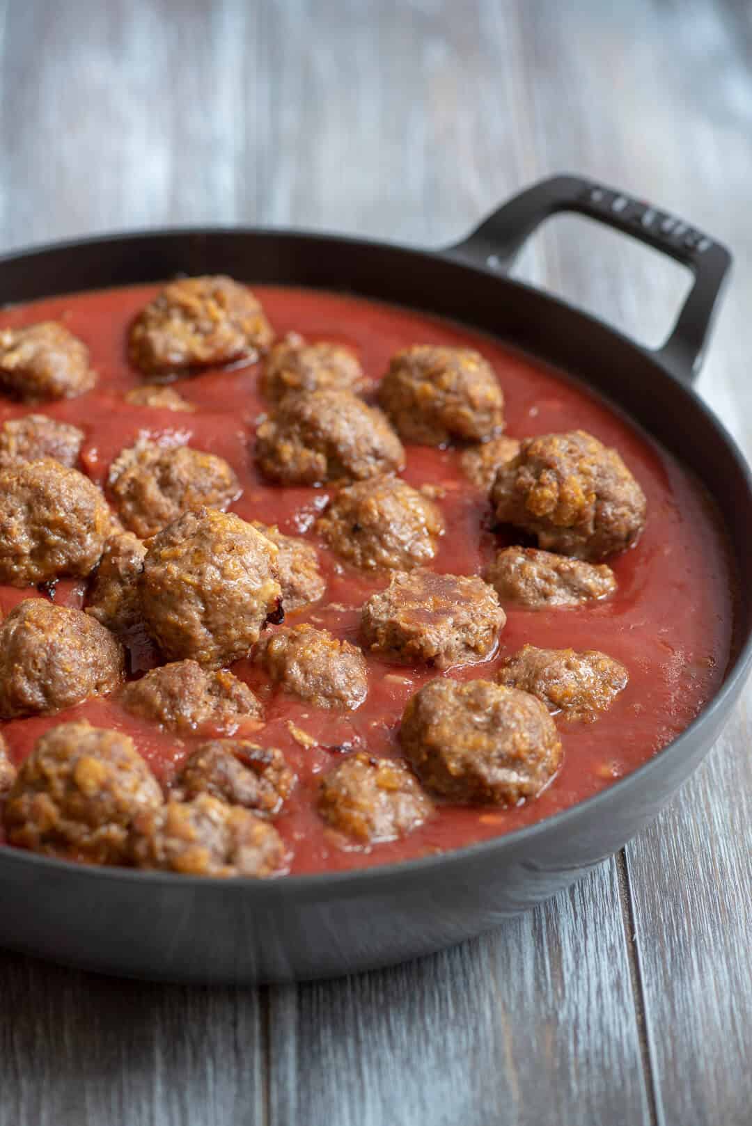 The cooked meatballs are placed into the sauce in the skillet.