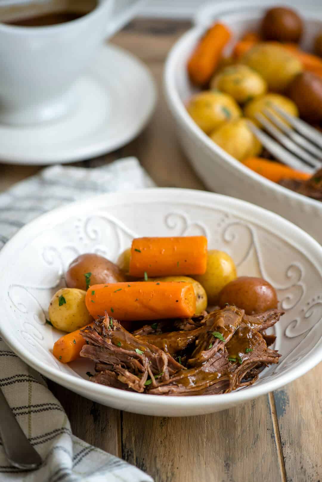 Instant Pot Pot Roast with carrots and potatoes in a white bowl.