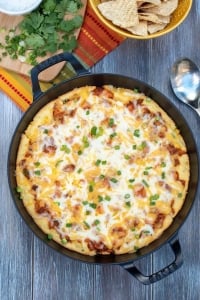 A cast iron skillet filled with cornbread topped with a cheesy chicken mixture.