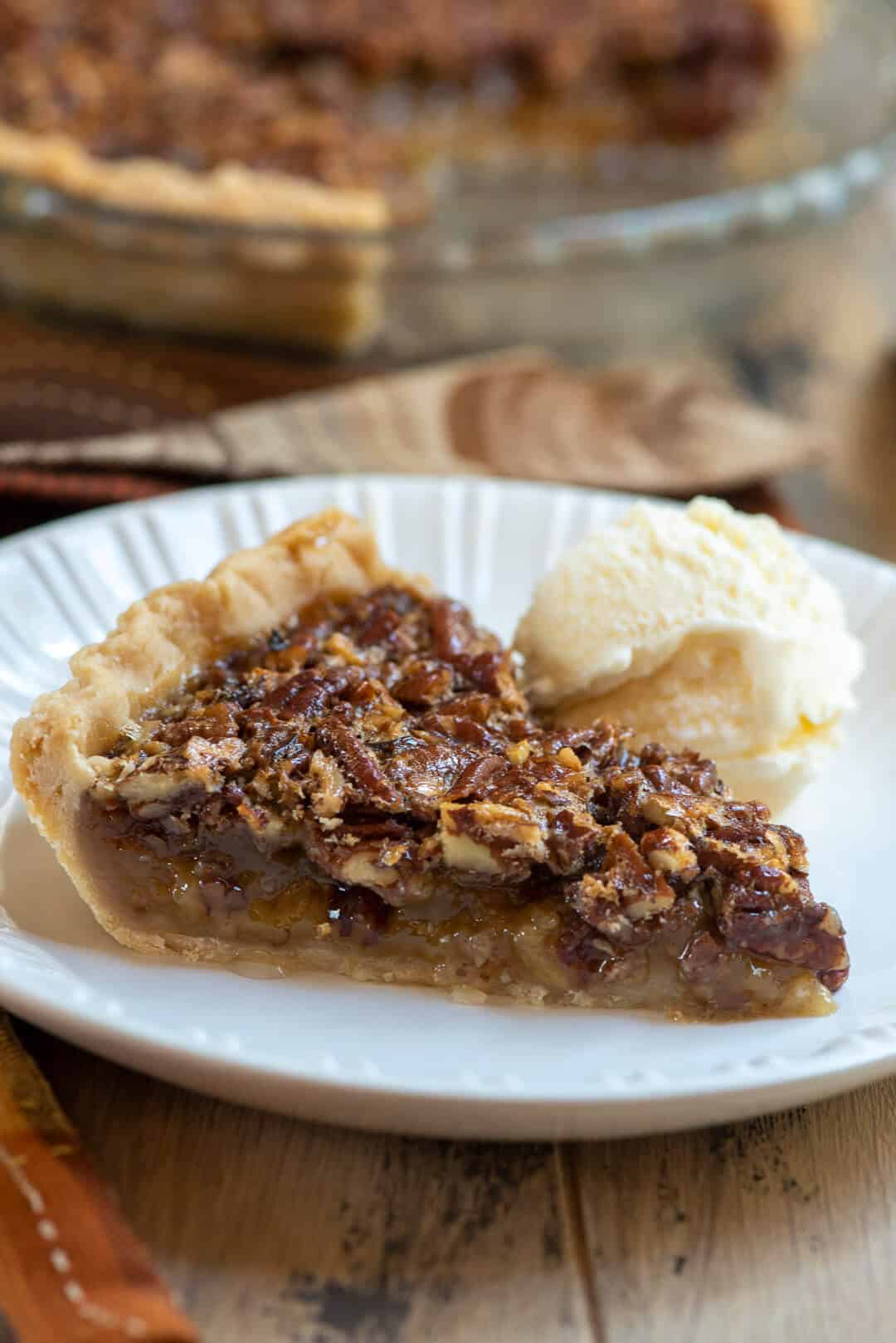 A slice of pecan pie on a white plate with a scoop of vanilla ice cream.