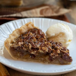 A slice of pecan pie on a white plate with a scoop of vanilla ice cream.