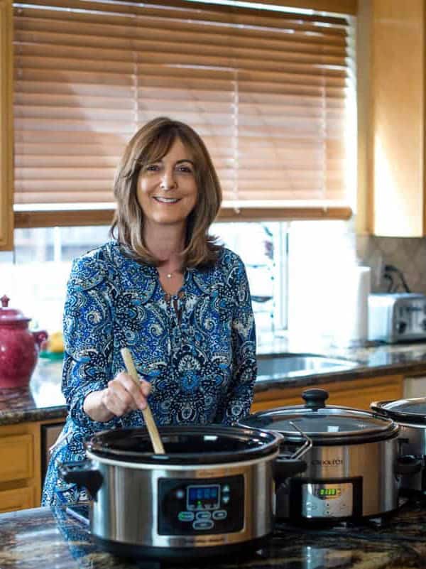 A woman preparing food in a slow cooker in a kitchen.