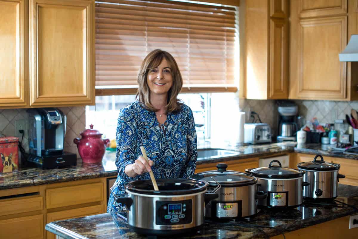 A woman preparing food in a slow cooker in a kitchen.