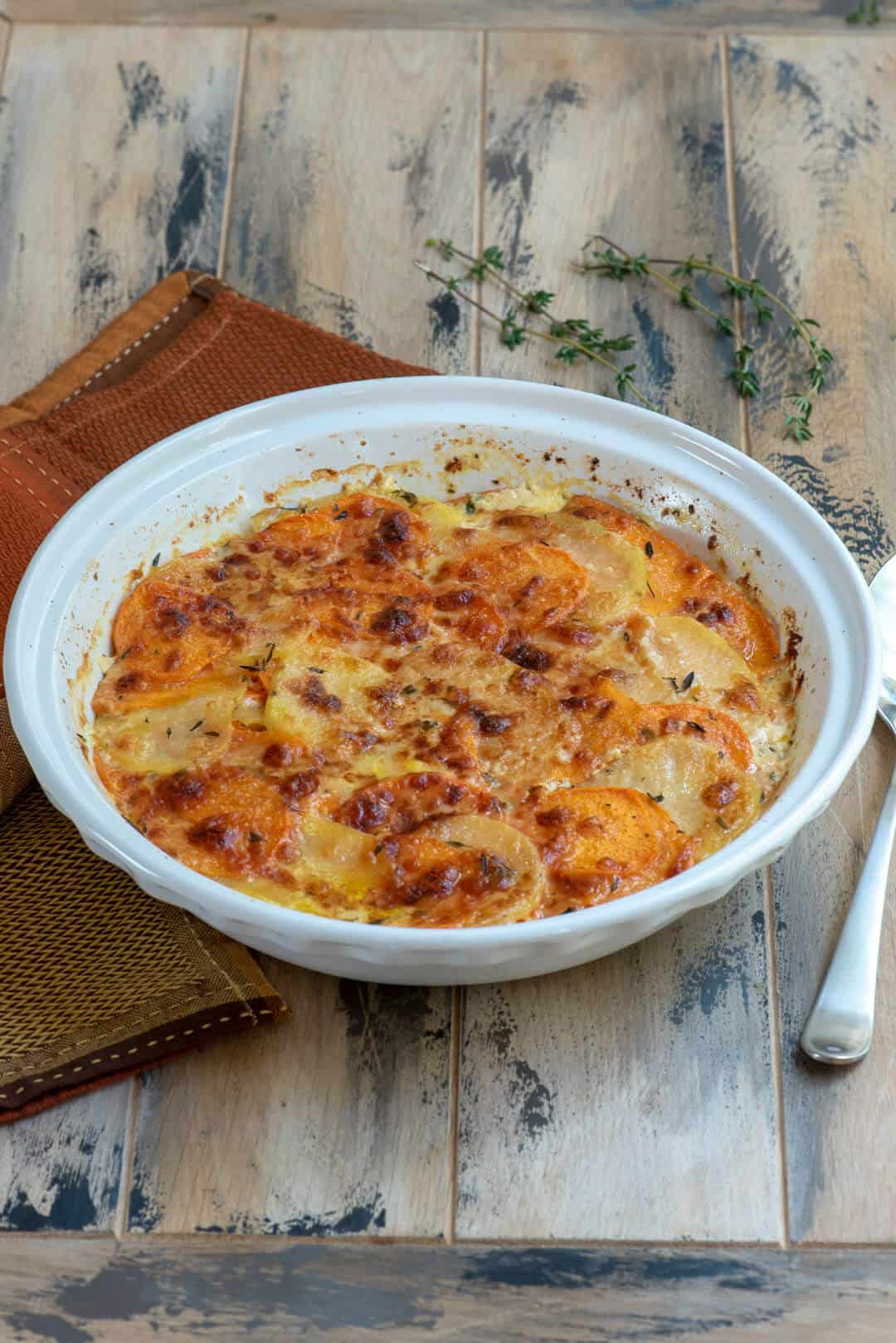 Sweet Potato Gratin in a round white baking dish on a orange and brown cloth.
