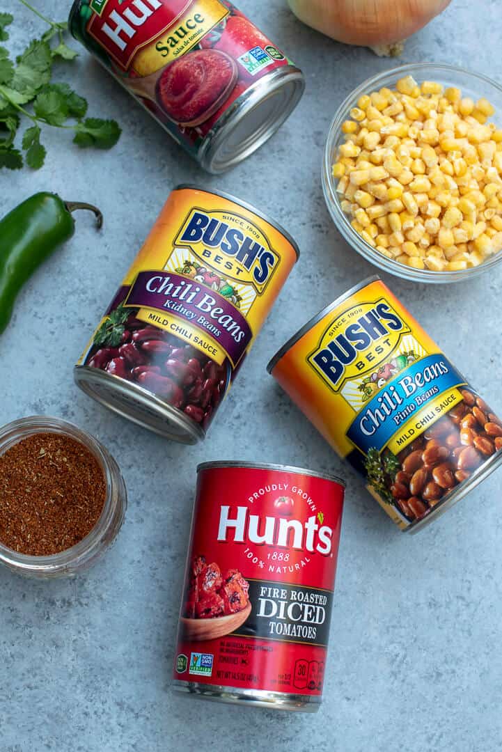 Cans of BUSH'S Beans, Hunt's Fire Roasted Diced Tomatoes, fire-roasted diced tomatoes and tomato sauce and small bowl of yellow corn.