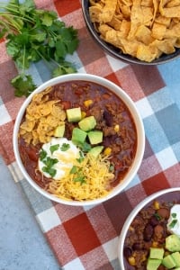 A bowl of chili topped with cheese, avocado, sour cream, and crushed corn chips.