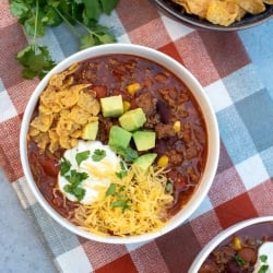 A bowl of chili topped with cheese, avocado, sour cream, and crushed corn chips.