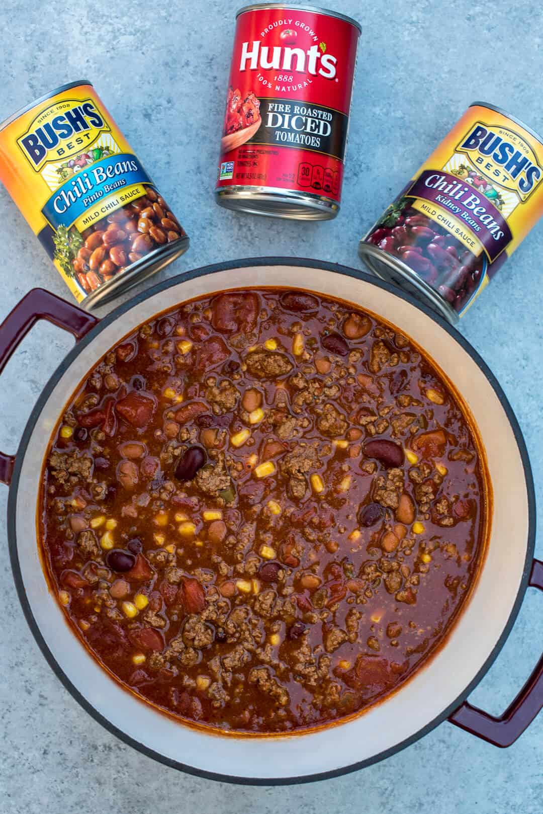 A Dutch oven full of chili with cans of beans and tomatoes in the background.