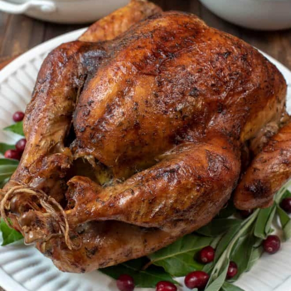 A browned turkey on a platter with fresh herbs and cranberries.