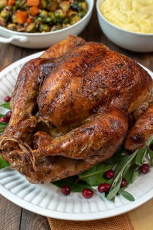 A Dry Brine Roasted Turkey on a white serving platter with fresh bay leaves and cranberries.