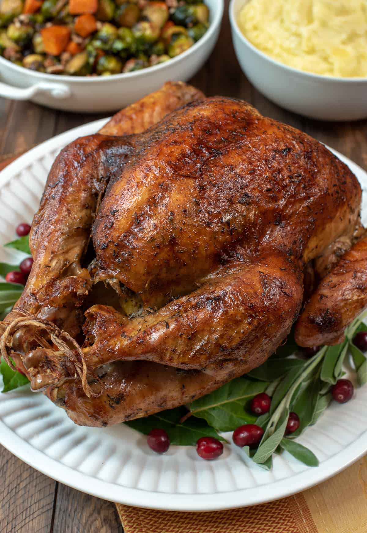 A Dry Brine Roasted Turkey on a white serving platter with fresh bay leaves and cranberries.