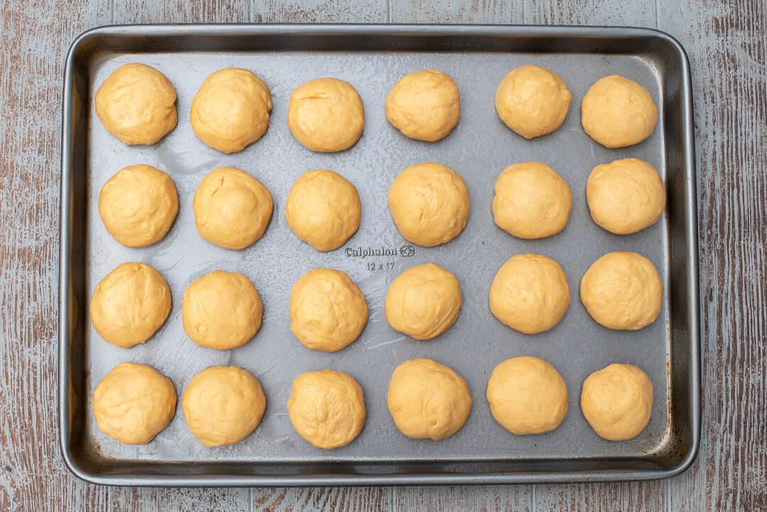 24 even sized balls of dough on a baking sheet.