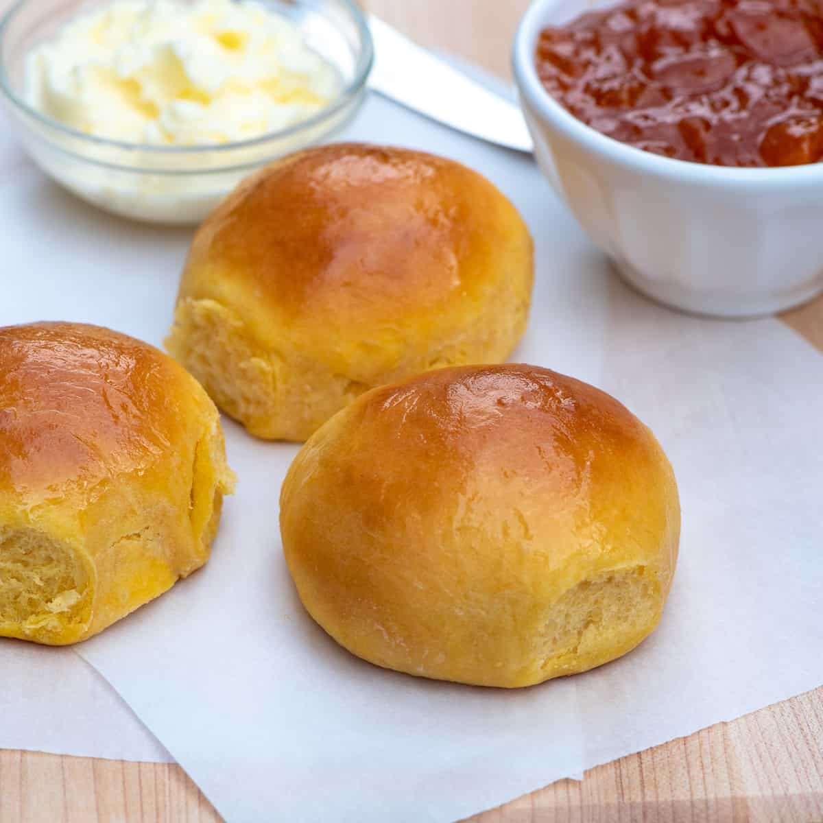 Three sweet potato rolls with bowls of butter and jam in the background.