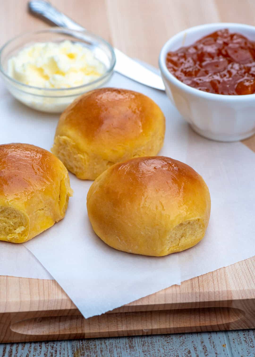 The rolls on a cutting board with a small bowl of jelly and butter in the background.