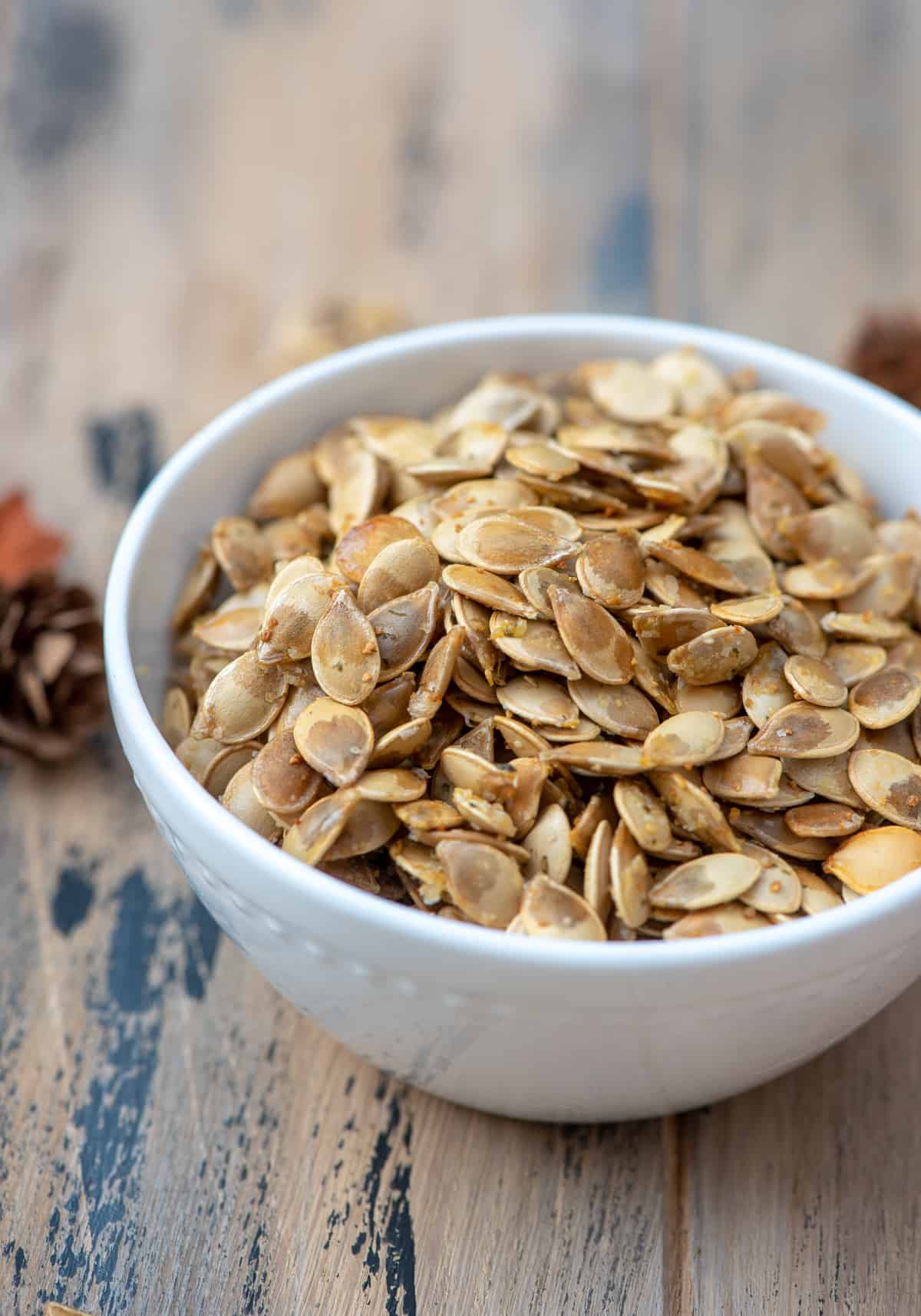 A side view of a white bowl filled with roasted acorn squash seeds.