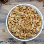 A top down shot of a bowl of roasted acorn squash seeds on a brown ball with fall leaves and pine cones.