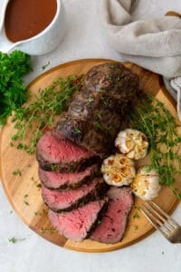 An over the top shot of sliced beef tenderloin with garlic on a wood platter.