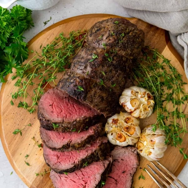 An over the top shot of sliced beef tenderloin with garlic on a wood platter.