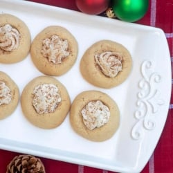 White thumbprint cookies filled with a creamy filling and dusted with nutmeg on a white platter.