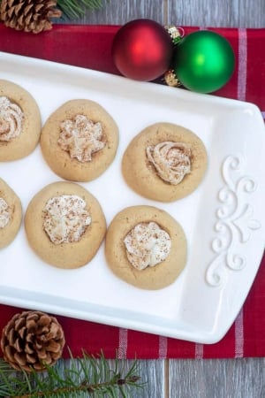 White thumbprint cookies filled with a creamy filling and dusted with nutmeg on a white platter.