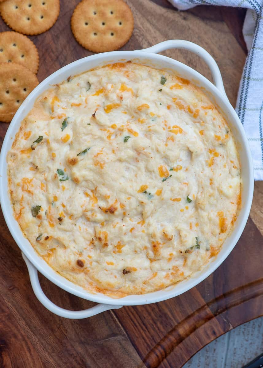 A top down shot of crab dip in a white serving bowl with Ritz crackers scattered around it.