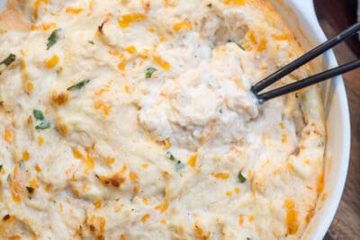 A top down shot of a small spoon resting in a white bowl filled with cheesy crab dip.