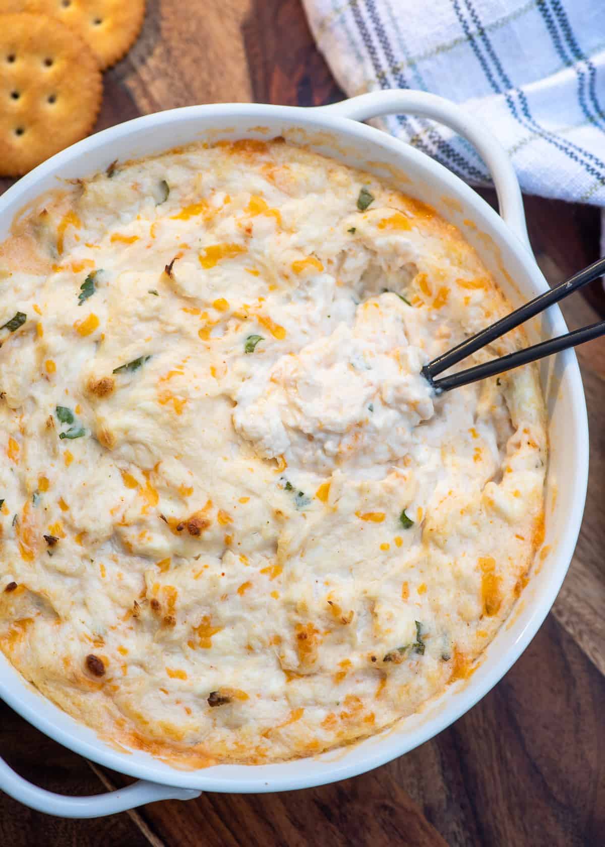 A top down shot of a small spoon resting in a white bowl filled with cheesy crab dip.