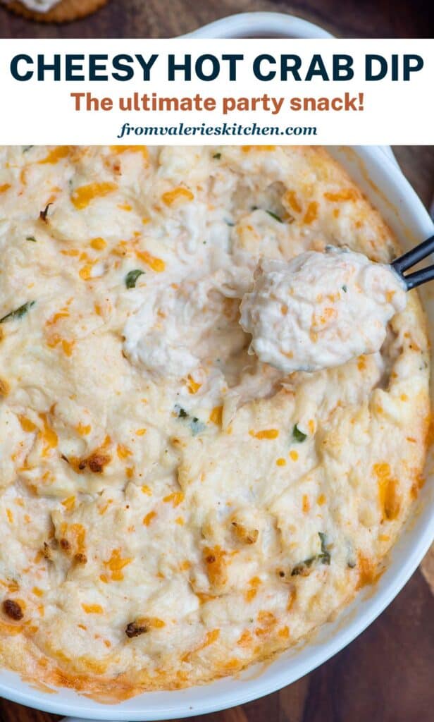 A small spoon scoops cheesy hot crab dip from a white bowl with text.