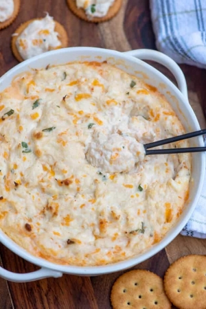 A white bowl filed with crab dip with a spoon.