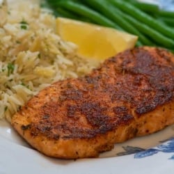 A piece of blackened salmon on a plate with rice and a slice of lemon.
