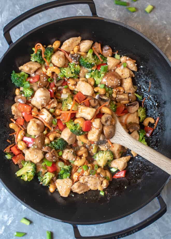 A wooden spoon lifts a spoonful of Cashew Chicken from the wok.